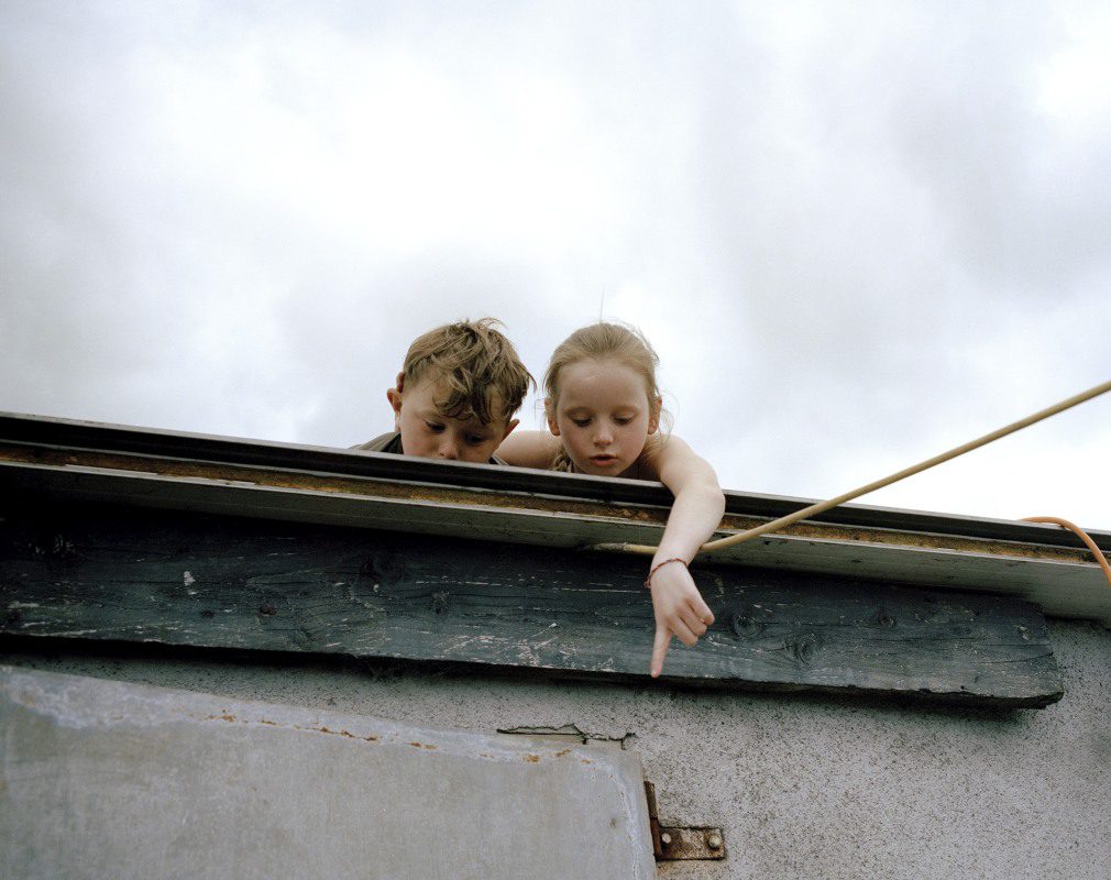 Two children on a flat roof looking down and pointing. 